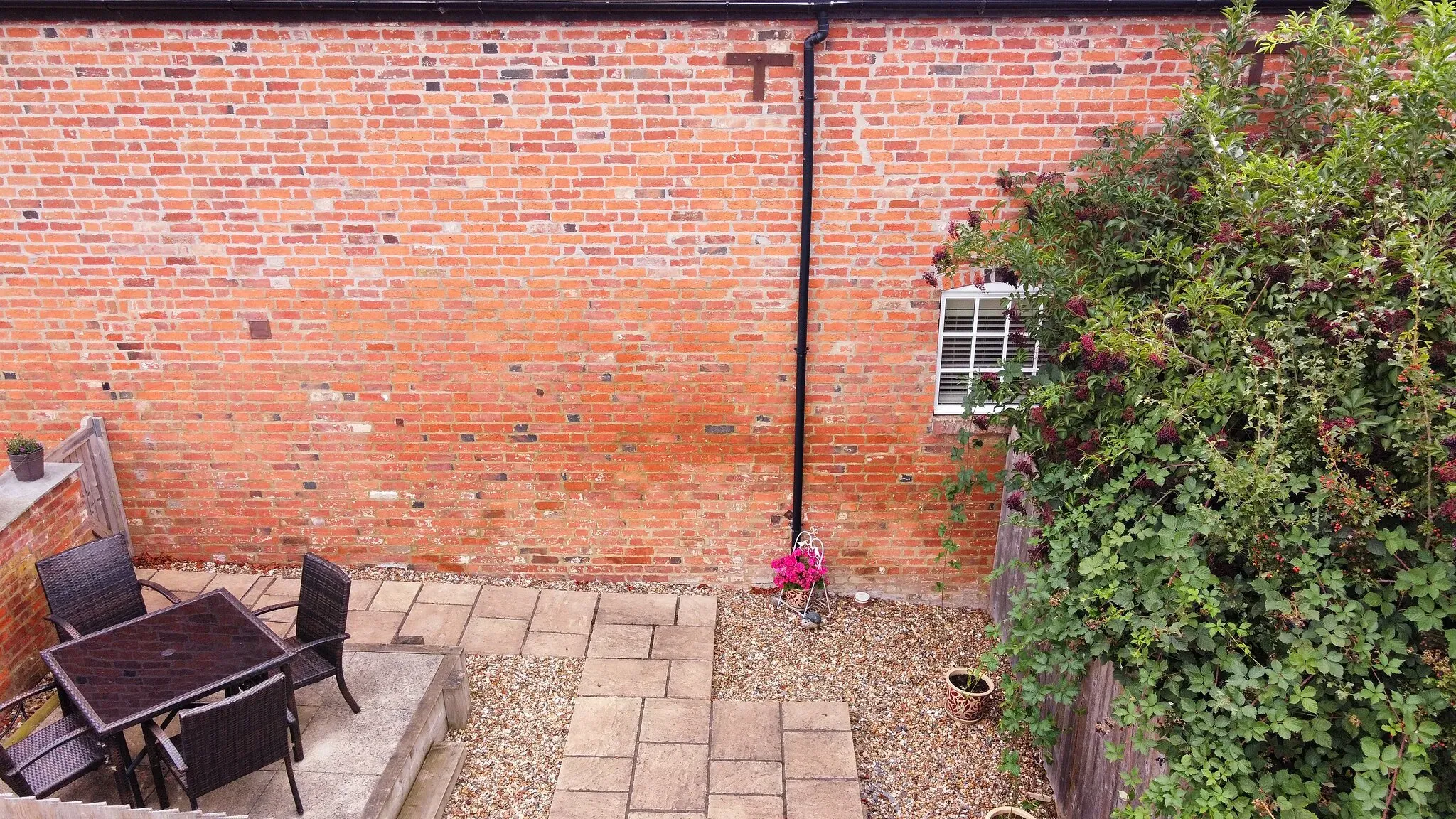 Private patio with rattan table and four chairs against the old brick barn wall
