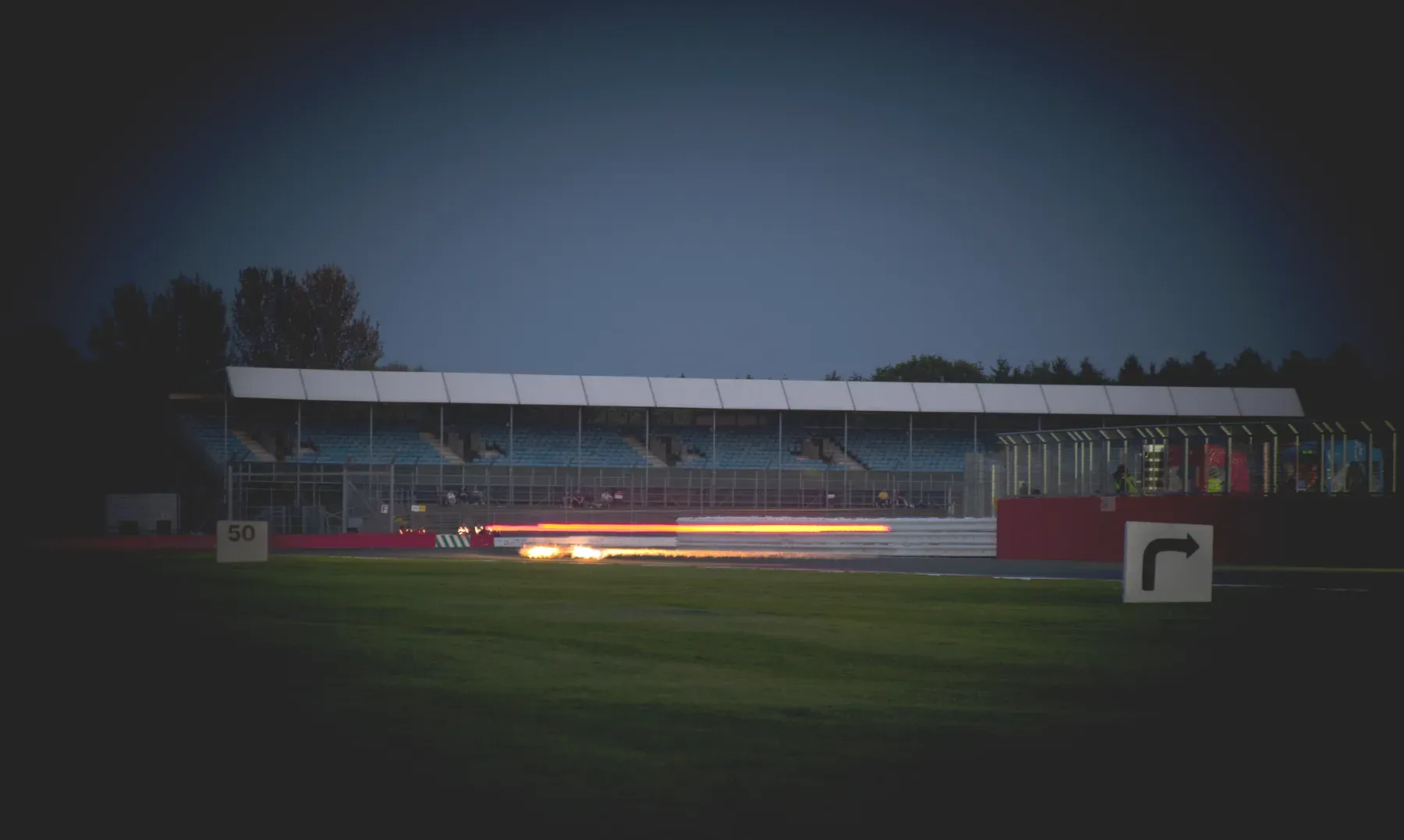 A car streaking past the grandstand at Silverstone Circuit under a darkening sky